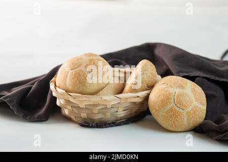 Delicious freshly baked buns placed in wicker bowl near brown fabric against white background Stock Photo