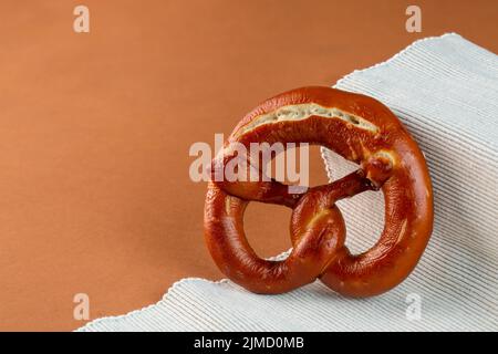 Delicious freshly baked pretzel with dark crust served on ribbed fabric against brown background Stock Photo