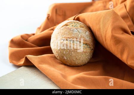 Loaf of tasty fresh bread placed on orange fabric in bakery Stock Photo