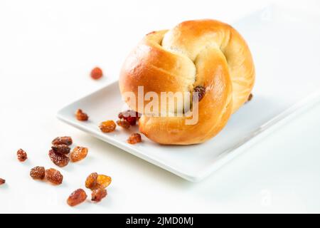 From above delicious twisted bun served with sweet raisins on rectangular plate on white background Stock Photo
