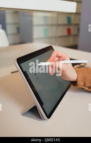 Unrecognizable woman with stylus making notes on tablet while doing homework assignment in library in daytime Stock Photo