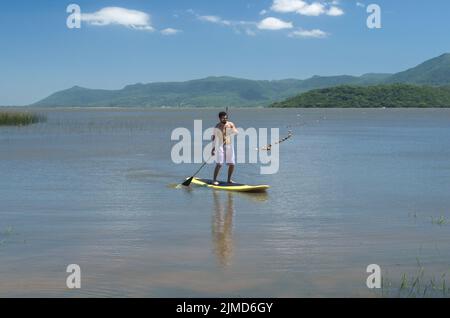 Young man practicing Stand Up Paddle on lake, yellow board, paddling. Paddleboarding. Stock Photo