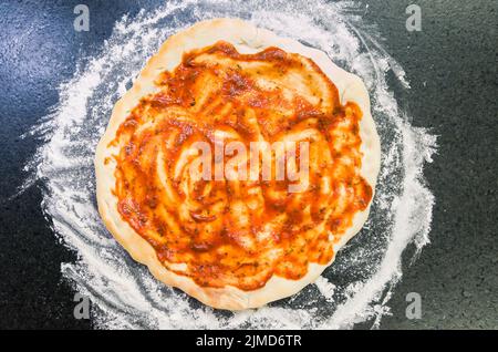 Preparing pizza, close-up of pizza dough with tomato sauce. Stock Photo