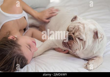 Beautiful woman sleeping in bed with english bulldog puppy. Stock Photo