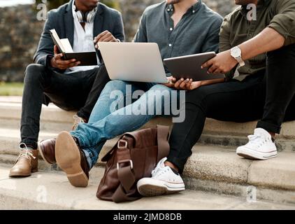 Whatever our location, lets get it done. a group of businessmen sitting on stairs and using a laptop during a meeting against a city background. Stock Photo