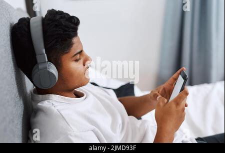 This app has the biggest selection of songs Ive ever seen. a young man using his cellphone while listening to music through his headphones. Stock Photo
