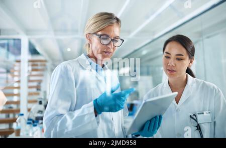Using multiple resources to test new methods. two scientists working together on a digital tablet in a lab. Stock Photo