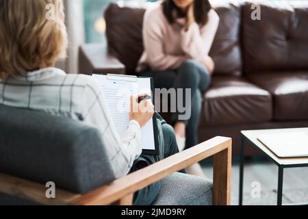 Keep talking until the answers become clearer. a psychologist writing notes during a therapeutic session with her patient. Stock Photo
