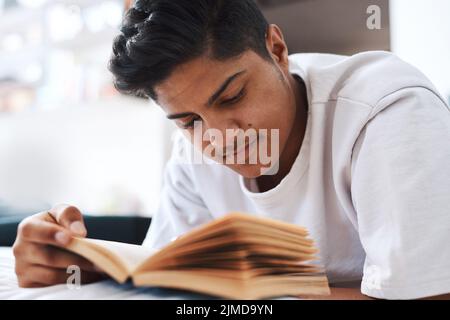 Ill probably read this book again. a young man reading a book while lying on his bed. Stock Photo