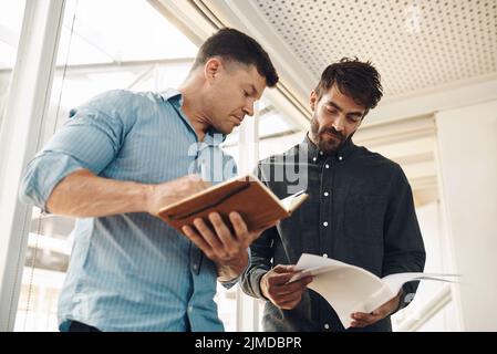 Comparing notes. two handsome young businessmen looking over their notes after a successful meeting in the boardroom. Stock Photo