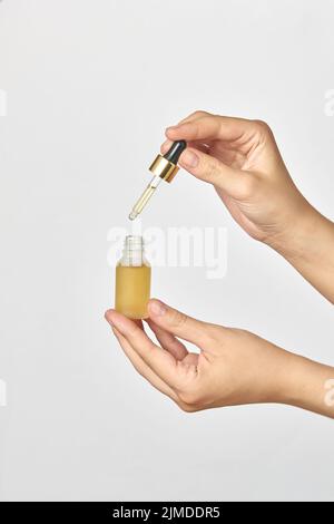 Bottle and pipet of medical cannabis CBD oil in hands against a light grey background. Stock Photo