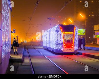 Moscow.Russia. December 26, 2019. Trams in the fog lit by a network of LEDs arrive at a bus stop with passengers. Environmentall Stock Photo