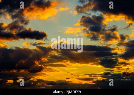 A very dramatic sky full of yellows, blues and oranges. Contrasting clouds during sunset illuminated by the setting sun. Bright Stock Photo