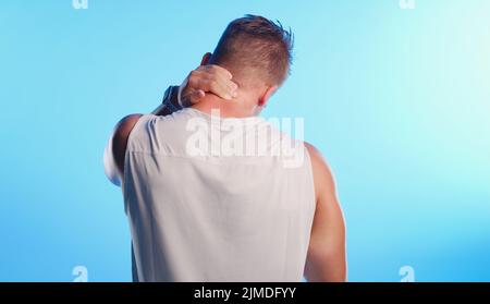 He may have overdid it a little. Rearview shot of an unrecognizable young man rubbing his neck in pain against a blue background. Stock Photo