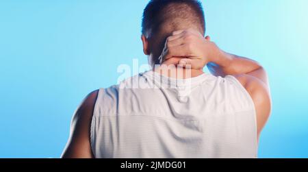 It can be a painful experience. Rearview shot of an unrecognizable young man rubbing his neck in pain against a blue background. Stock Photo