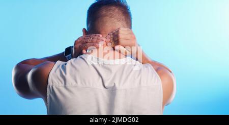 Injury is a risk of exercise. Rearview shot of an unrecognizable young man rubbing his neck in pain against a blue background. Stock Photo