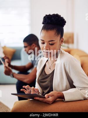 Technology keeps us connected. an attractive young businesswoman sitting and using a tablet while her colleagues work behind her. Stock Photo