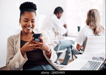 Responding to my text messages. an attractive young businesswoman sitting in her office with her coworkers and using her cellphone. Stock Photo