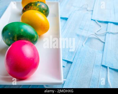 Colored Easter eggs on a white plate on a background of blue medical masks. Stock Photo