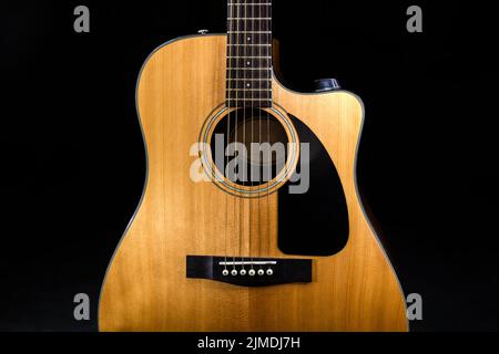 Body of a classic acoustic six-string guitar with a yellow sound board and black pickguard on isolated black background Stock Photo