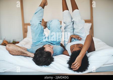 Playful interracial couple bonding while lying on a bed in a bedroom in the morning. Loving, resting and relaxing diverse lovers enjoying quality time Stock Photo