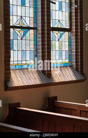 Wooden pews in an old Dutch church with a colorful stained glass window Stock Photo