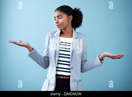 Confused and serious businesswoman with open hands or palms emoji pose making a difficult decision about future career on blue background. Unsure Stock Photo