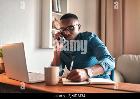 Young serious professional businessman talking on phone call, writing and sitting with digital laptop at home office. African american employee Stock Photo