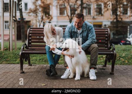 Husband and wife having rest on bench, caring of dog Stock Photo