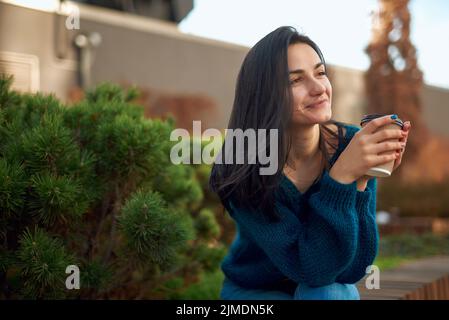 Dreamy female enjoying hot drink in a cosy city park Stock Photo