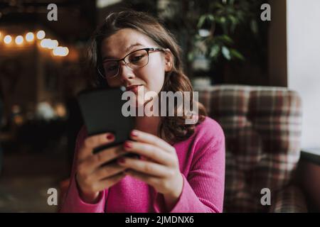 Pretty young woman is using smartphone indoors Stock Photo