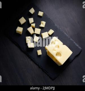 Semi-hard cheese with holes, maasdam on black plate Stock Photo