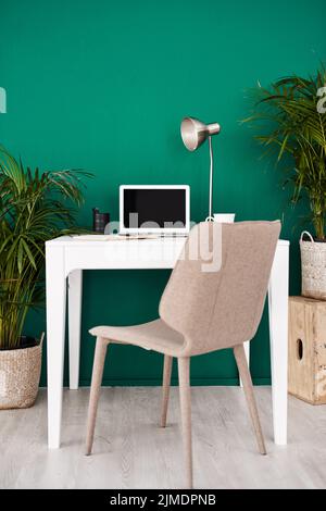 The space to get creative and productive. Still life shot of various items at a workstation against a green wall in an office. Stock Photo