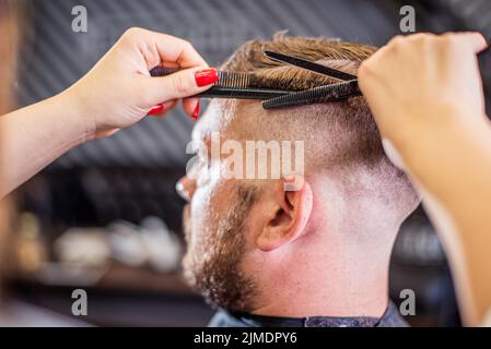 Beautiful hairdresser woman doing hairstyle to bearded man in barbershop Stock Photo