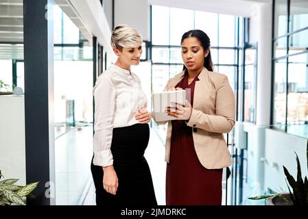 Collaboration is key in their industry. two businesswomen using a digital tablet together in an office. Stock Photo