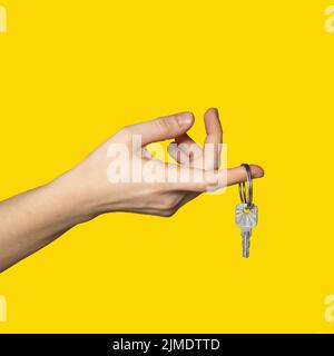 On finger of woman hand hangs key on bright yellow background. Stock Photo