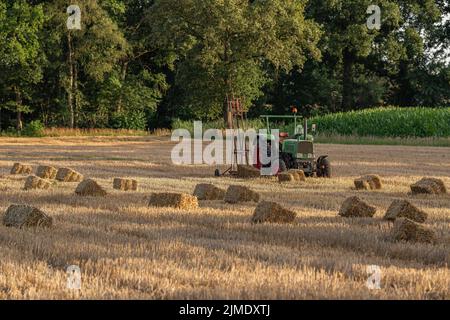 Old tractor in a field with straw bales Stock Photo