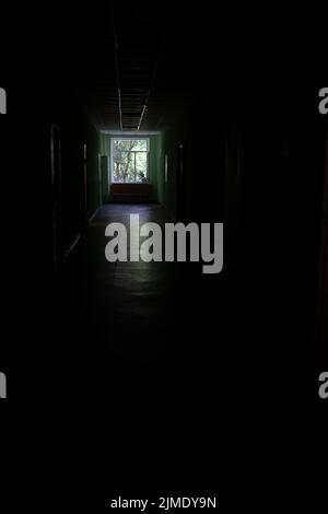 A window at the end of a dark, unlit corridor. Dark dark dark corridor of an abandoned building. Stock Photo