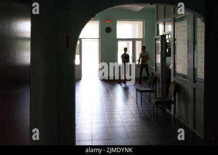 A door at the end of a dark, unlit corridor. Silhouettes of people in the backlight. Stock Photo