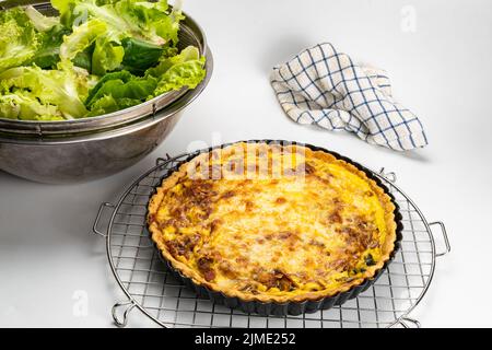 Freshly baked quiche  in black metal oven pie baking plate on a metal cooling rack. Stock Photo