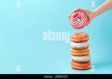 Stack of donuts, donut in hand on blue, copy space Stock Photo