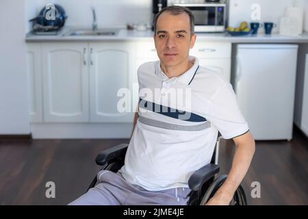Smiling Young Handicapped Man Sitting On Wheelchair In Kitchen Stock Photo