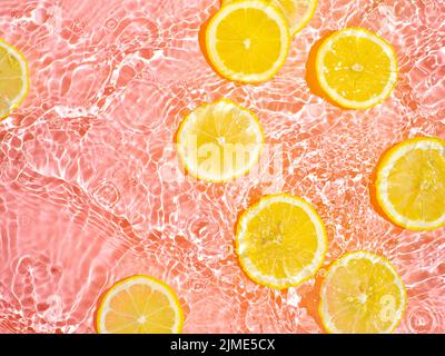 Lemon slices in clean transparent water, pink bg Stock Photo