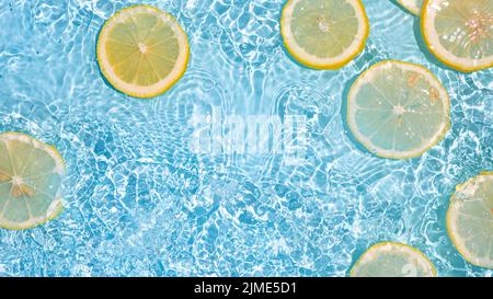 Lemon slices in clean transparent water, blue bg Stock Photo