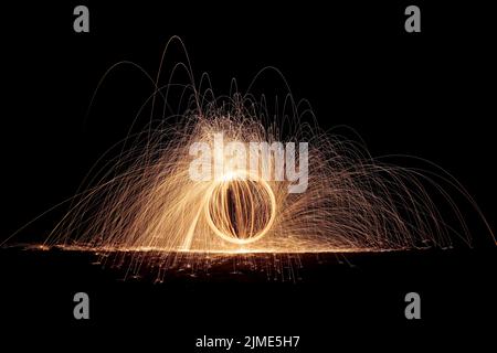 Steel wool spinning on a beach , throwing off yellow and orange sparks making a spinning pattern Stock Photo