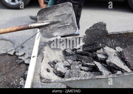 Construction waste trolley. Puts the asphalt into the cart with a shovel. Stock Photo