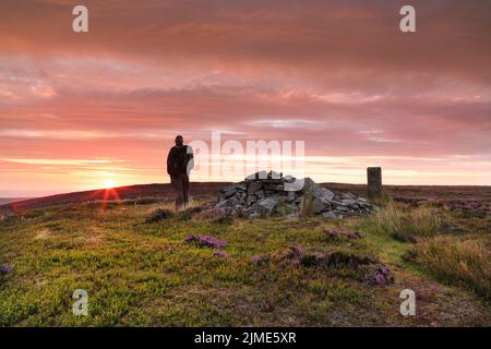 Long Man, Teesdale/Weardale border, County Durham, UK. 6th August 2022. UK Weather.  A beautiful sunrise illuminates the purple flowering heather surrounding the Currick of Long Man hill in the North Pennines this morning.  These stone curricks, also known as cairns, often act as markers on borders and hills in the North Pennines. Credit: David Forster/Alamy Live News Stock Photo