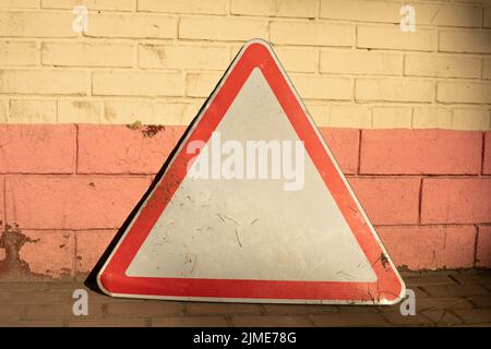 The road sign stands against the wall. The triangle symbolizes traffic. Stock Photo