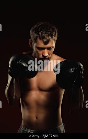 This is a dramatic portrait of a boxer in old boxing gloves on a dark background. An athletic mixed martial arts fighter Stock Photo