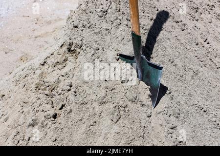 A scoom shovel sticks out of a pile of gray sand. building material. Concept of road or repair work. Stock Photo